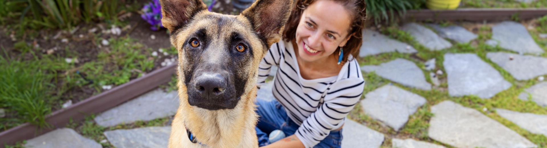 Smiling person sitting outside on a stone patio with a dog seated in front of them
