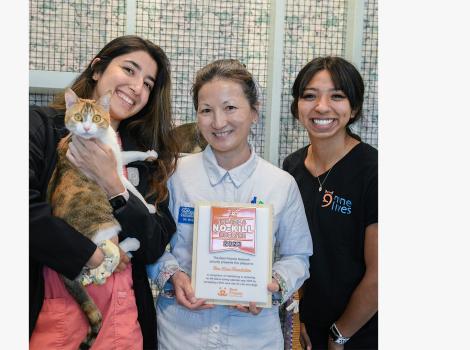 Three happy people posing with a calico cat and a Best Friends no-kill 2023 shelter trophy