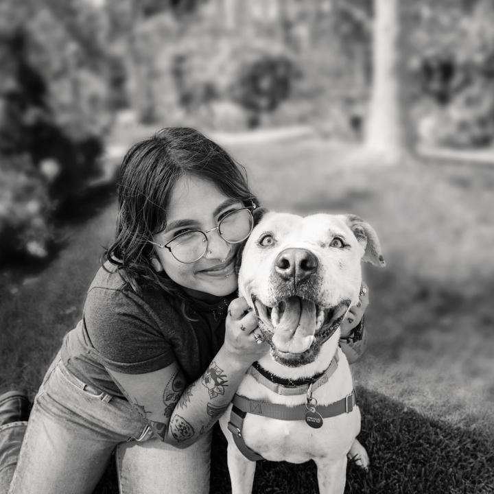 Smiling person sitting with a dog in the grass