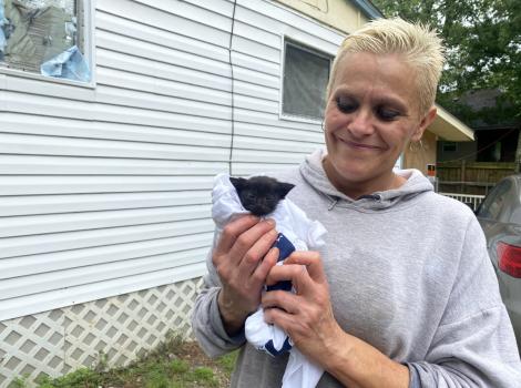 Smiling person holding a small black kitten, next to a mobile home