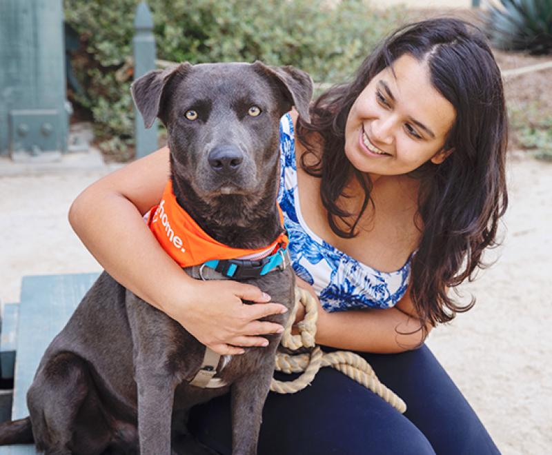 Smiling person outside with a leashed dog wearing a bandanna