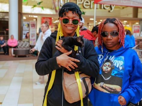 Two people in a shopping mall holding a black kitten