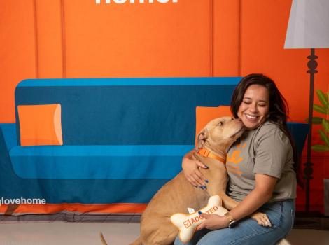 Sarah Shaw sitting on the ground with Peaches the dog in front of a backdrop of a couch and lamp
