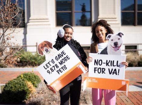 Two people outside holding signs at the Capitol in Richmond, Virginia