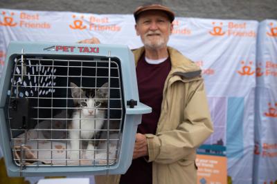 Person adopting a kitten in a carrier, in front of a Best Friends logo backgrop